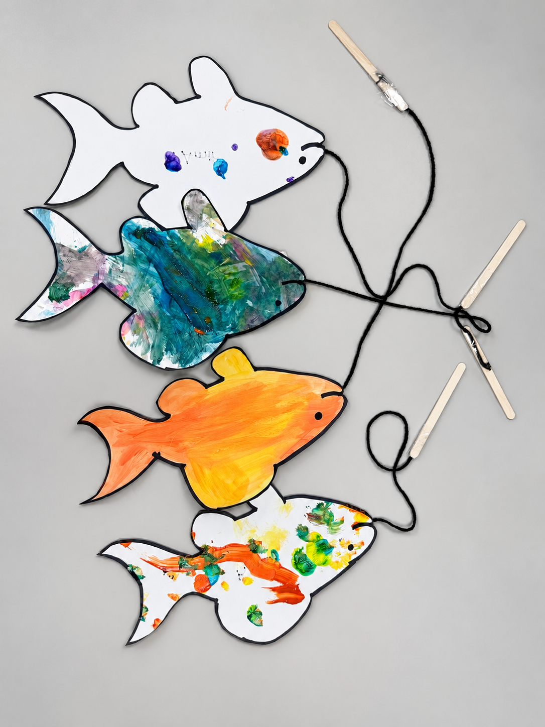 Painted fish cutouts with yarn fishing lines and craft stick fishing rods